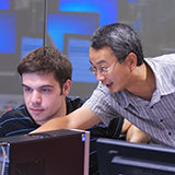 Kevin Du gestures toward a computer screen in a computer science classroom.
